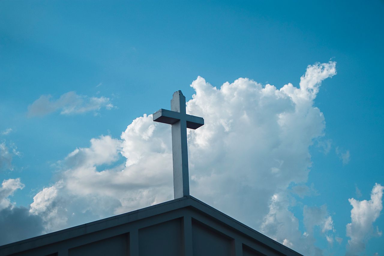 About Low angle view of a cross on a church roof with a vibrant blue sky and clouds.