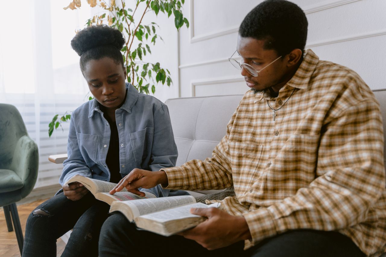 Services Two individuals engaged in reading the Bible together, depicting faith and togetherness.